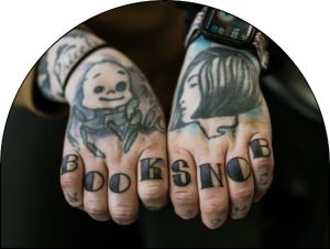 Two hands with freshly touched up tattoos on the fingers that say "Book Snob."