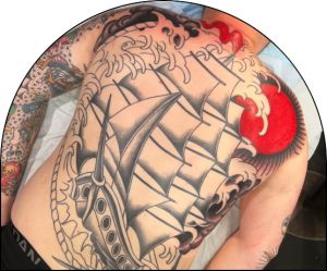 A very large tattoo on a client's entire back of a red and black tattoo of a large ship on the ocean with a red sun.