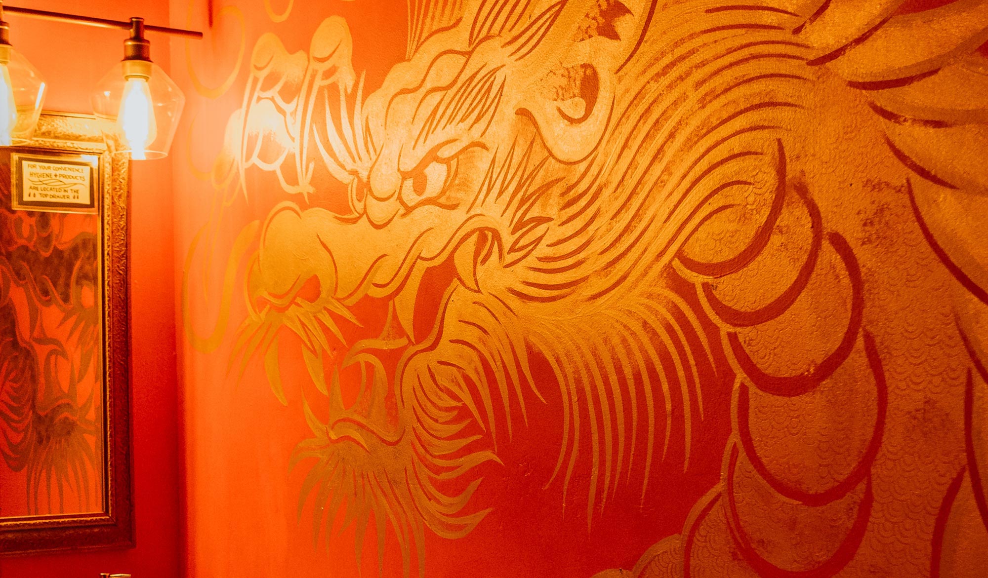 A gold Chinese Dragon mural painted on an orange-red wall.