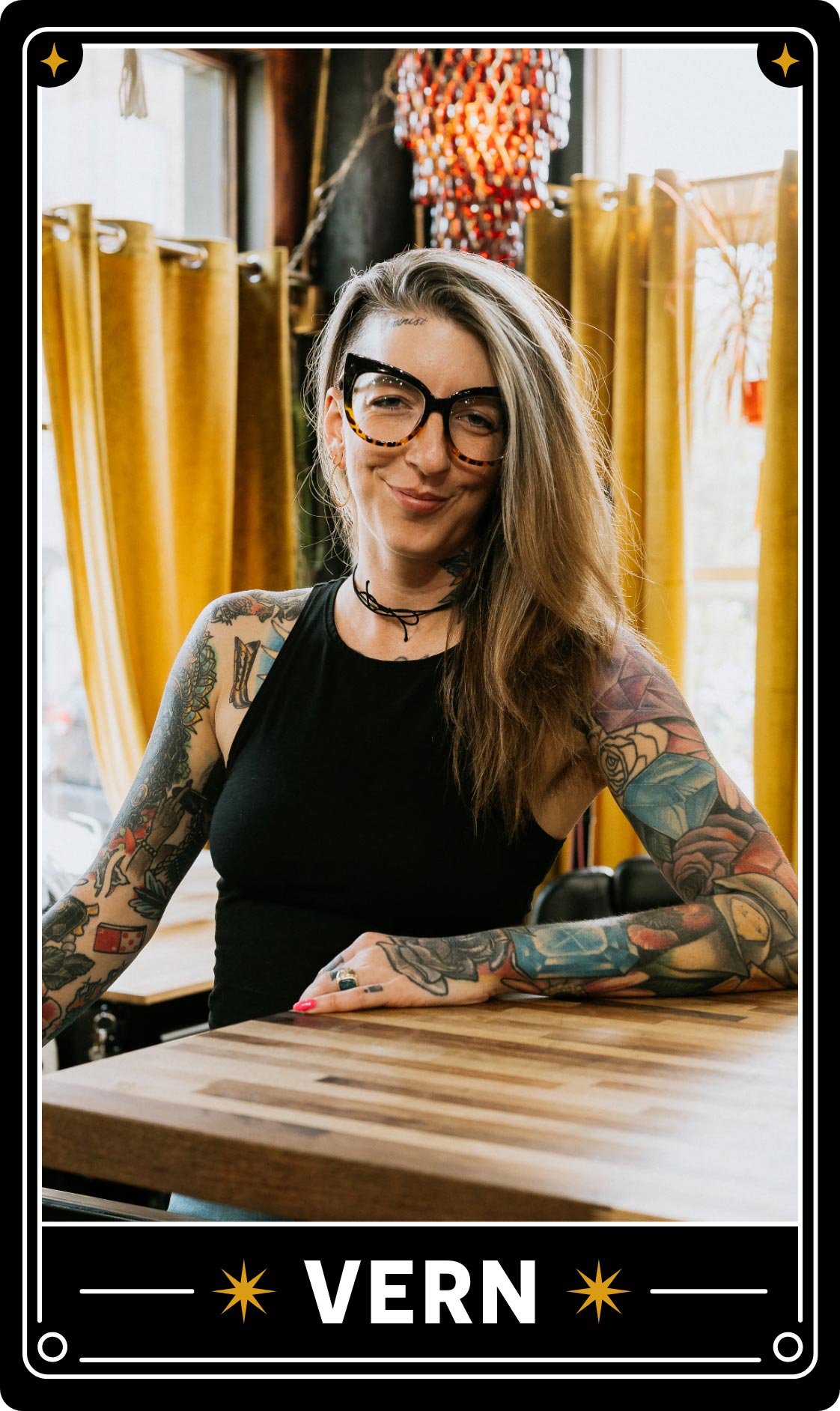 A black, white, and gold tarot card with an image of Veronica or Vern, the owner of Black Magic Tattoo, leans on a sunny counter inside the studio.